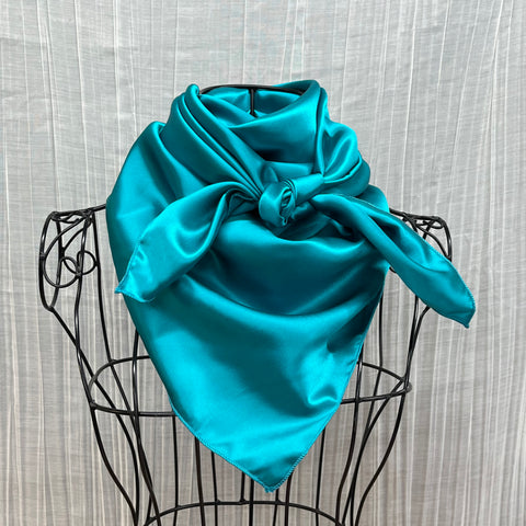 A teal silk scarf displayed on a black metal mannequin frame, with a textured white background.